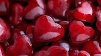 Red heart shaped candies in close up macro photography, glossy surface with romantic Valentine's Day appeal, sweet treats on dark background.