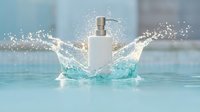 White cosmetic pump bottle with dynamic water splash creating crown effect in turquoise pool water. Luxury skincare product photography for spa and wellness brands.