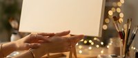 Artist hands creating artwork on canvas with warm bokeh lights and paintbrushes in cozy studio setting for creative projects and artistic inspiration.