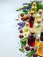 Natural essential oils in glass bottles with cork stoppers surrounded by fresh herbs, spices and dried orange slices for aromatherapy and wellness treatments.