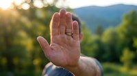 Close-up of an open palm raised against a sunlit mountain landscape, symbolizing stop gesture, peace, or greeting. Suitable for safety, communication, and wellness concepts.