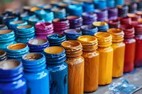 Vibrant rows of colorful paint bottles arranged in spectrum order from blue to orange and red, showing artistic supplies with textured paint residue on caps.