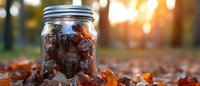 Glass mason jar filled with autumn leaves on fallen foliage ground with warm golden sunset light creating bokeh background for seasonal decoration.