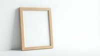 Empty wooden picture frame leaning against white wall, mockup template for artwork display, home decor and interior design projects.