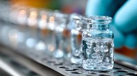Glass vials with liquid samples in laboratory setting, shallow depth of field focus on transparent container with bubbles, scientific research background.