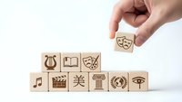 Hand placing wooden cube with theater mask among blocks featuring arts symbols on white background for creative education concepts.