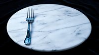 Elegant marble round table with single fork on dark background, fine dining and upscale restaurant concept for hospitality design.