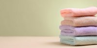 Stack of folded pastel colored bath towels in pink, beige, purple and mint green on neutral background for spa, bathroom or hotel amenities.