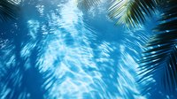 Dreamy underwater view through palm leaves with sunlight creating rippling patterns on blue water surface, evoking tropical paradise atmosphere.