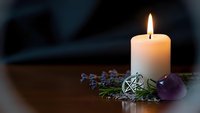 Burning white candle with pentagram pendant, amethyst crystal and dried lavender on wooden surface creating mystical spiritual atmosphere for meditation rituals.