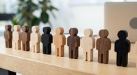 Wooden human figures in diverse colors arranged in row on desk representing teamwork, diversity, inclusion and unity in workplace or community setting.