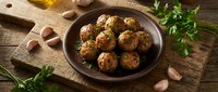 Homemade meatballs with herbs served in rustic ceramic bowl on wooden cutting board with fresh parsley and garlic cloves for cooking and dining.