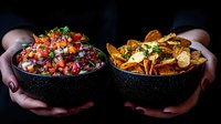 Fresh homemade pico de gallo salsa and crispy tortilla chips served in black stone bowls against dark background, hands holding traditional Mexican appetizers.