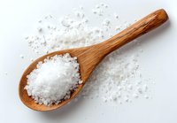 Wooden spoon with coarse sea salt crystals on white background, scattered salt grains surrounding the spoon.