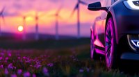 Modern luxury car parked in blooming purple wildflower field at sunset with wind turbines silhouettes in background creating dramatic atmospheric scene.