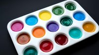 Watercolor paint palette with sixteen vibrant colors in white tray, isolated on dark background. Suitable for art education, creative projects, painting tutorials, and design resources.