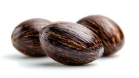 Fresh whole nutmeg seeds with dark brown striated surface on white background, macro food photography showing natural spice texture and pattern.