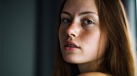 Young Caucasian woman with brown hair looking directly at camera with natural lighting creating dramatic shadows on face for portrait photography.