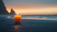 Glowing orange candle on sandy beach at sunset with dramatic coastal cliffs silhouetted in background, creating peaceful meditation atmosphere.