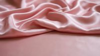 Soft pink silk fabric with elegant flowing folds and luxurious texture for fashion design, textile backgrounds, and romantic decor projects.