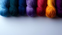 Colorful yarn skeins arranged in rainbow order from blue to purple on white background, perfect for knitting and crochet projects.