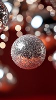 Sparkling silver Christmas ball ornament with glitter texture against blurred festive bokeh lights on dark red background, creating magical holiday atmosphere.