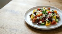 Colorful salad with roasted vegetables, feta cheese, and fresh herbs served on white plate over wooden table surface for culinary and food styling.