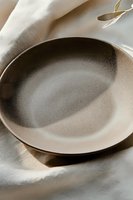 Empty ceramic plate on white linen tablecloth with soft natural lighting and shadows creating minimalist dining atmosphere for food photography and restaurant menus.
