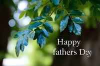 Fresh green leaves with water drops against blurred bokeh background and Happy Father's Day text overlay, natural greeting card design concept.