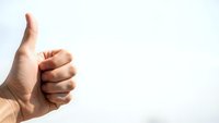 Hand showing thumbs up gesture against white background expressing approval, success and positive feedback for business presentations.