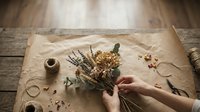 Florist arranging dried flowers and lavender on kraft paper with twine and natural materials on wooden table for craft and design projects.