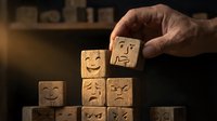Hand placing wooden cube with happy face emoji among blocks showing various emotions for customer satisfaction and feedback concept.