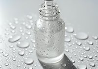 Clear glass dropper bottle with water droplets on surface, showcasing skincare serum or essential oil product for beauty and wellness applications.
