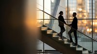 Two business professionals climbing modern office stairs with city skyline view during golden hour for corporate success and career advancement concepts.
