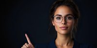 Young mixed race businesswoman wearing glasses gestures with raised finger against dark background, expressing confident professional leadership.