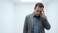 Stressed middle-aged Caucasian businessman in gray suit touching forehead showing headache, fatigue or mental pressure in modern office environment.