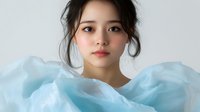 Young Asian woman with natural makeup and updo hairstyle wrapped in flowing light blue fabric against white background, soft ethereal portrait with gentle expression.