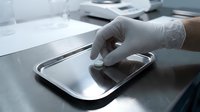 Healthcare professional wearing latex gloves handling sterile medical instrument tray in clinical laboratory or hospital setting for surgical preparation and infection control.