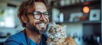 Caucasian bearded man in glasses holding fluffy Persian cat while smiling at home. Warm atmospheric lighting creates cozy mood for pet care and lifestyle content.