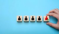 Hand selecting red person icon from row of wooden blocks showing recruitment and talent acquisition process on blue background.