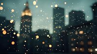 Blurred city skyline silhouette at dusk with glowing bokeh lights and raindrops on window glass creating dreamy urban atmosphere for background designs.