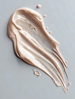 Creamy beige foundation or concealer smear with textured streaks and droplets on light gray background, cosmetic product texture for beauty and makeup industry.