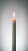 Single white candle burning with bright flame against soft gray background for meditation and relaxation concepts.