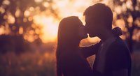 Romantic couple silhouettes kissing at golden hour sunset with warm bokeh lights creating intimate atmosphere for love and relationship concepts.