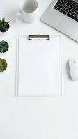 Clean white office workspace with blank clipboard, laptop, coffee mug, succulents and computer mouse on desk for business planning and productivity.