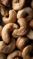Macro shot of roasted cashew nuts showing detailed texture and natural patterns. Close-up view highlights rich golden brown color and curved shapes on dark background.