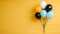 Festive balloon bunch in black, white, orange and blue against vibrant yellow wall background with copy space for party or celebration design.