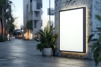 Illuminated blank white billboard mockup on concrete wall at dusk with decorative plant, urban setting background. Modern advertising display space.