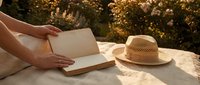Woman reading book outdoors in golden sunlight with straw hat on blanket during peaceful summer afternoon relaxation moment.