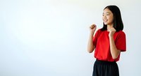 Young East Asian woman wearing bright red shirt and dark skirt, smiling while gesturing with fist raised in confident, empowered pose against white background for motivational content.